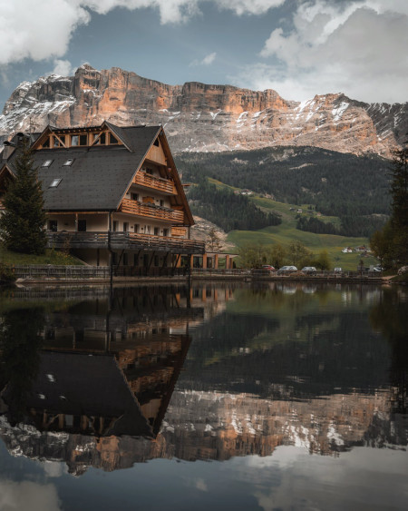 Sas dla Crusc mountain at a distance and a chalet hotel reflected in Lago Sompunt, South Tyrol, northern Italy