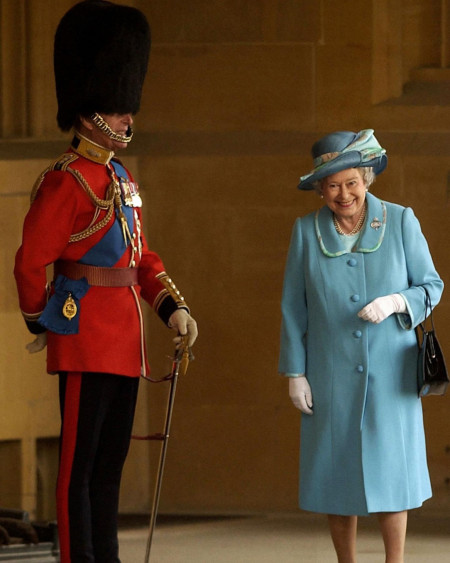 Queen Elizabeth II giggling as she walks past her husband Prince Philip in his full uniform