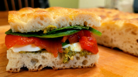 Homemade focaccia with pesto, mozzarella, torn basil, roasted red peppers, and spinach