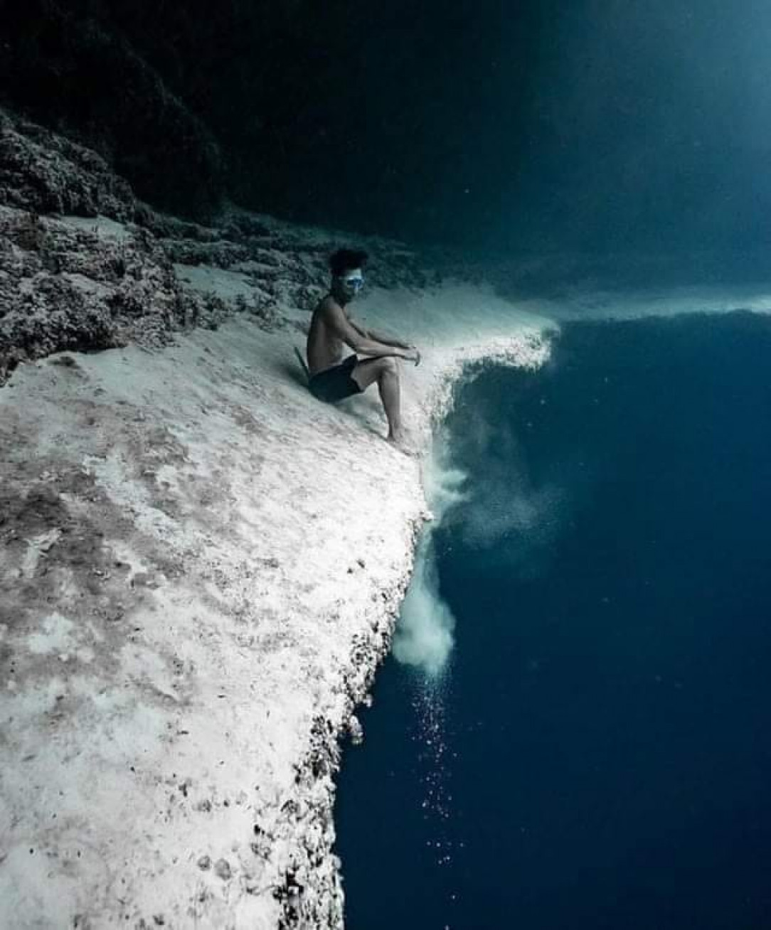 Diver sitting on the edge of underwater sea cliff
