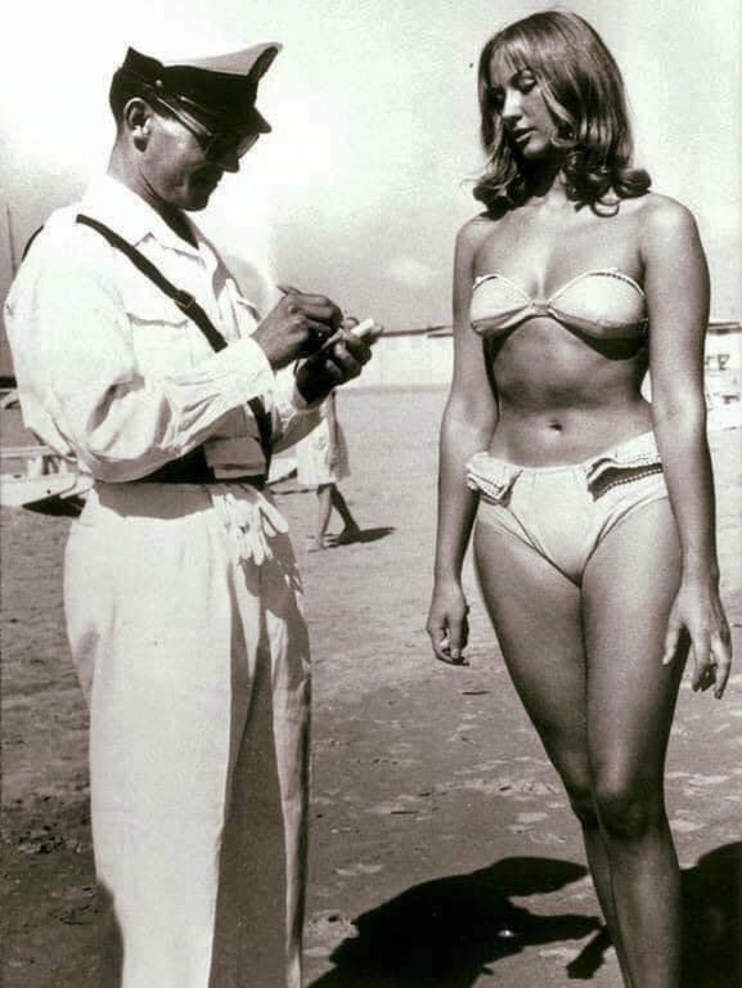 A police officer ticketing a woman for wearing a bikini on a beach, which was illegal at the time in Italy, 1950s