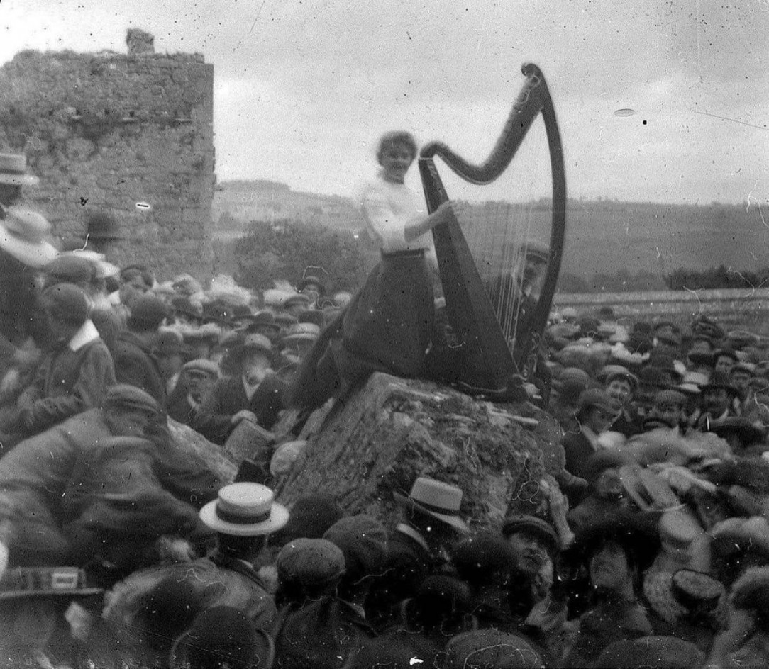 A young lady playing a large harp to the crowd in 1910 Ireland