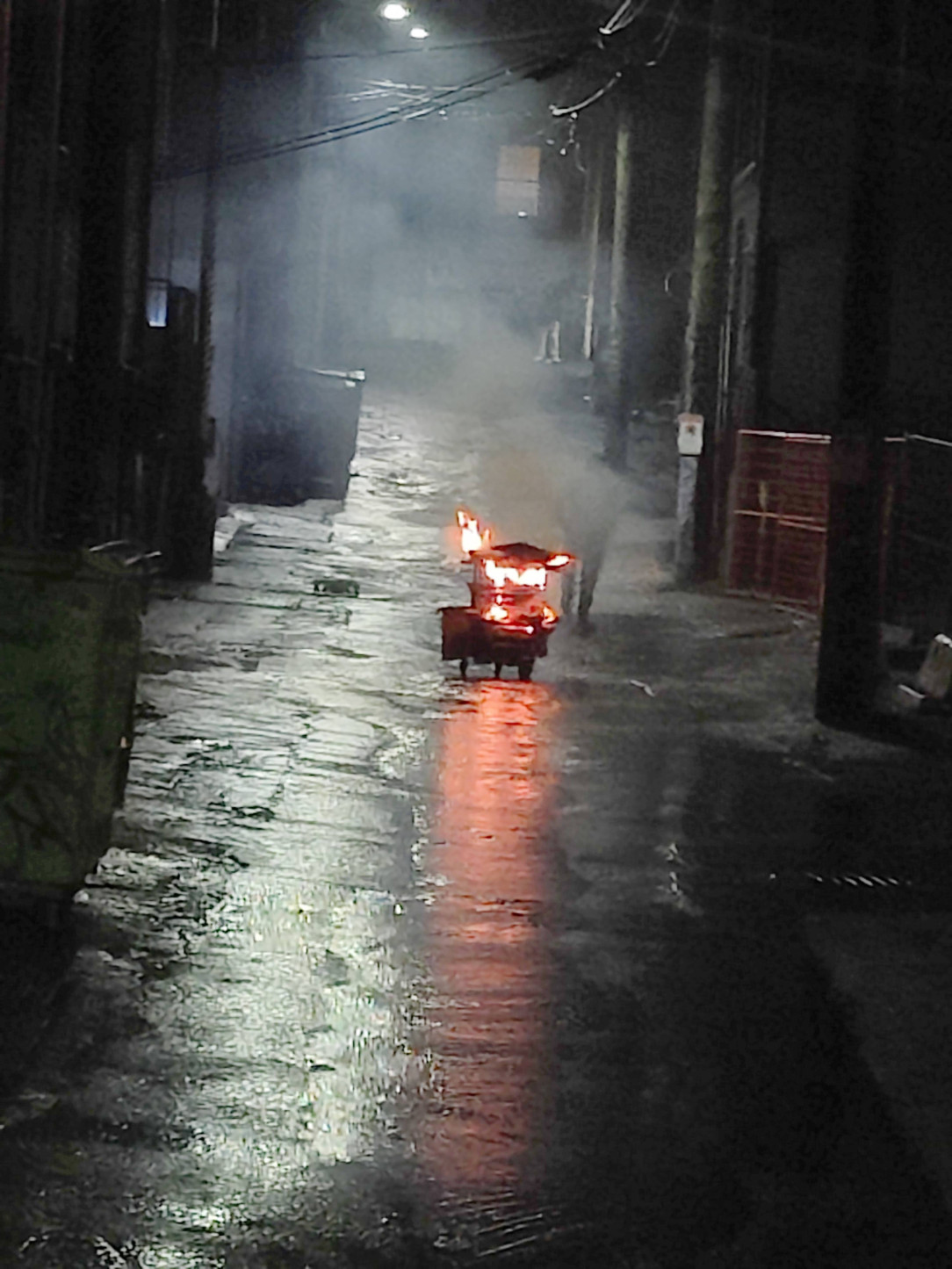 Man pushing a flaming shopping cart down an alleyway in Vancouver
